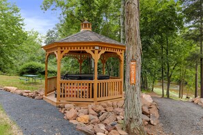 Un gazebo in legno con una panchina, circondato da rocce e alberi.