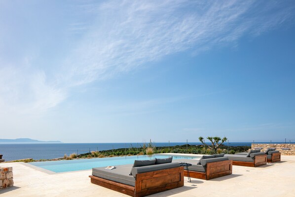 Un espace aménagé au bord de la piscine, avec des sièges extérieurs et une vue sur la mer.