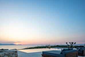 Une vue sur le coucher de soleil depuis un espace aménagé près de la piscine, avec des chaises longues et un mur en pierre.