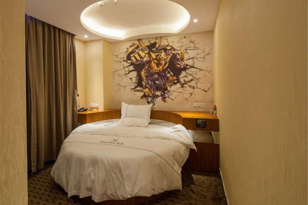 A hotel room with a bed, a desk, a chair, a wall art piece, and a curtain.