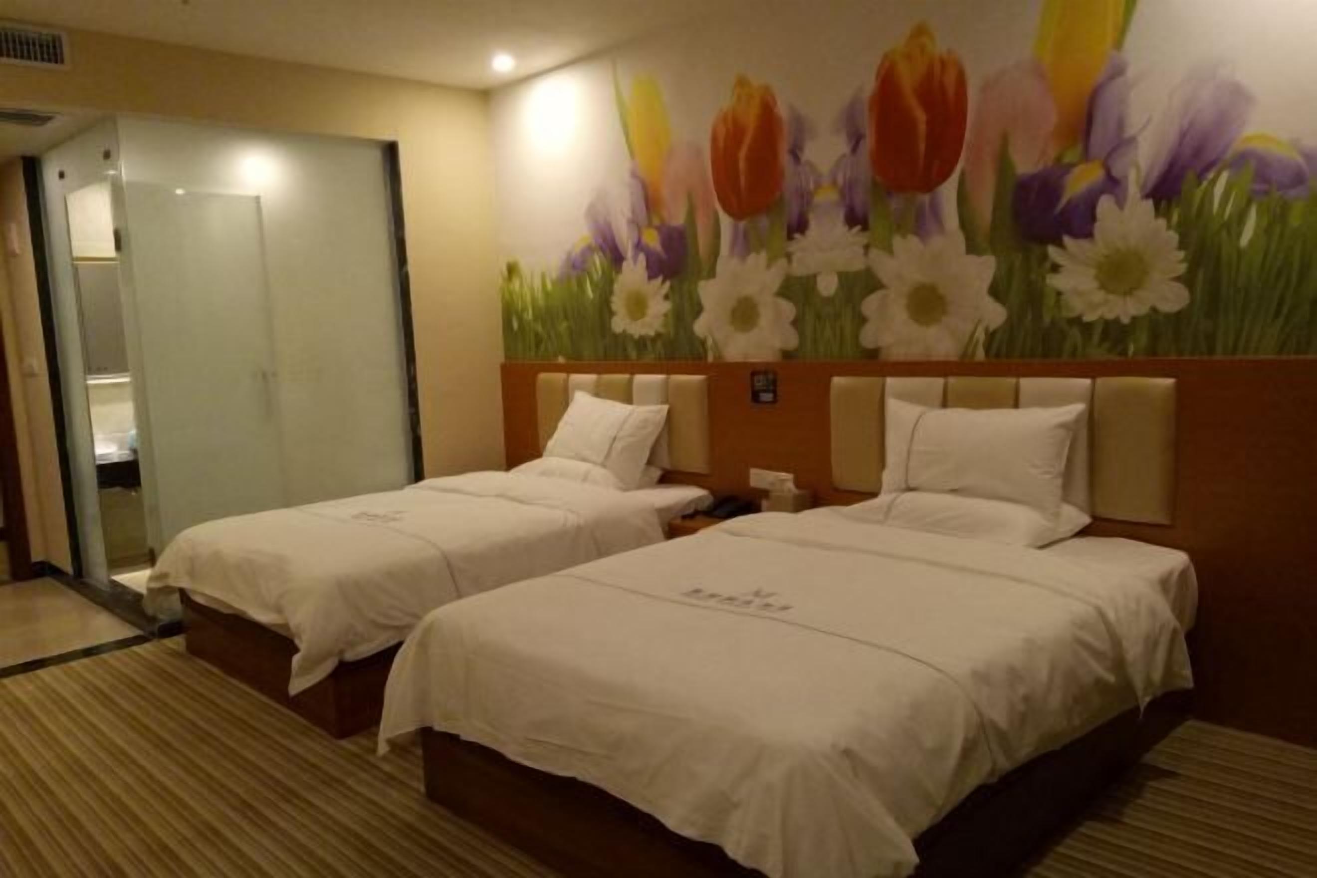 Quarto de hotel com duas camas, banheiro e um mural de flores na parede.