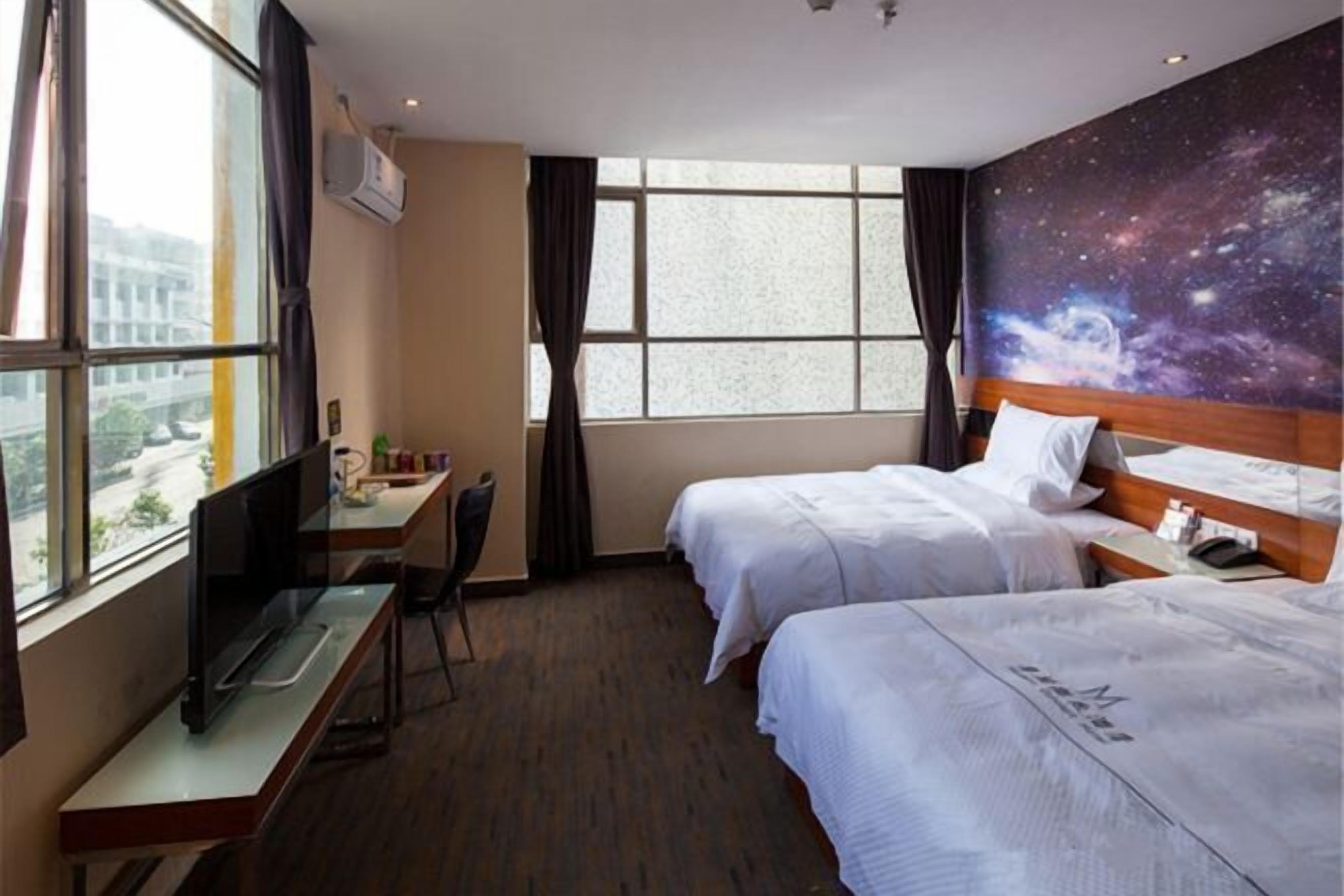 A hotel room with two beds, a desk, a chair, and a large window with a view of the city.