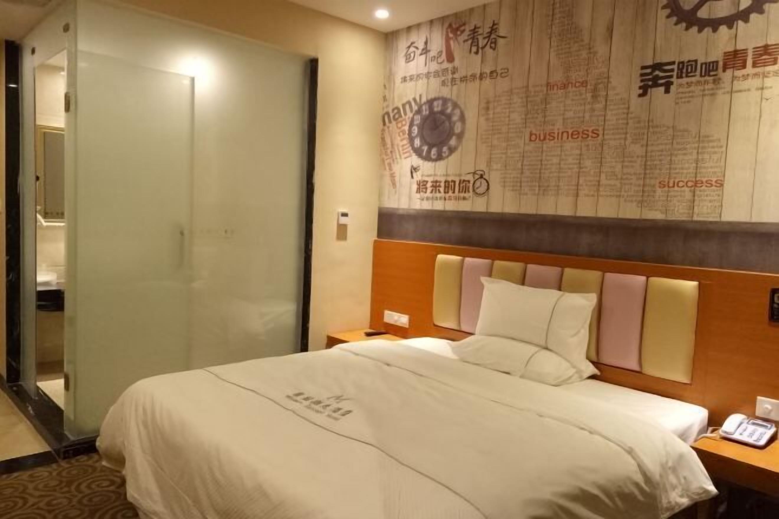 A hotel room with a bed, a nightstand, and a wall with motivational text and a clock.