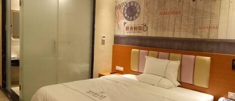 A hotel room with a bed, a nightstand, and a wall with motivational text and a clock.
