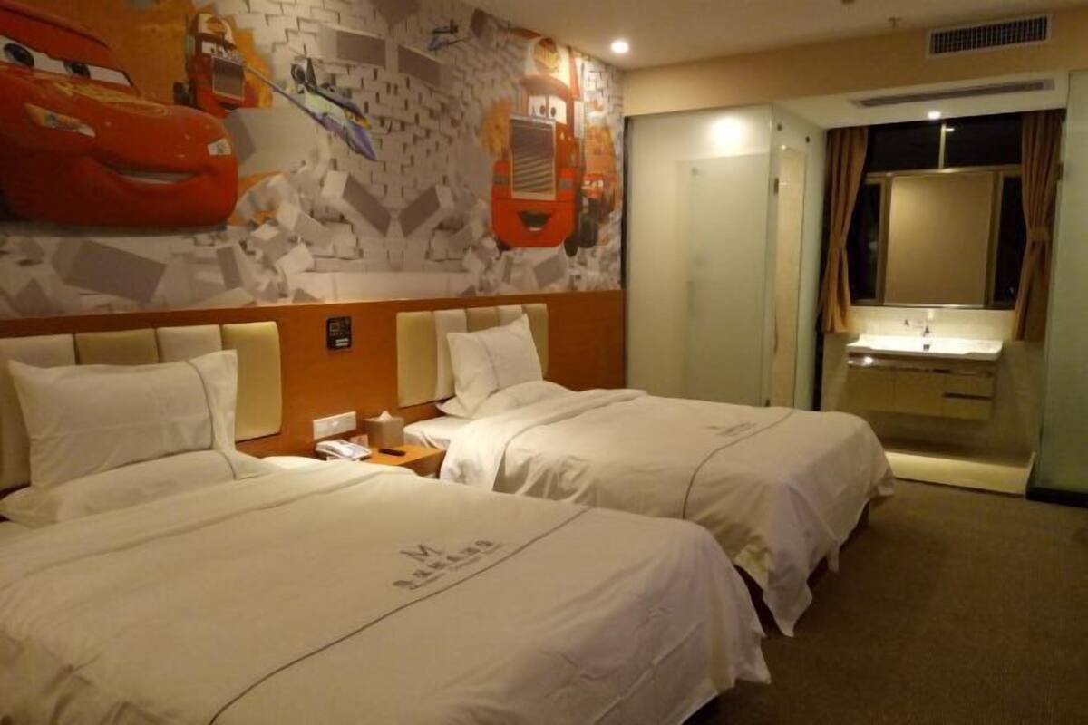 A hotel room with two beds, a wall mural, a bathroom with a sink, and a window with curtains.