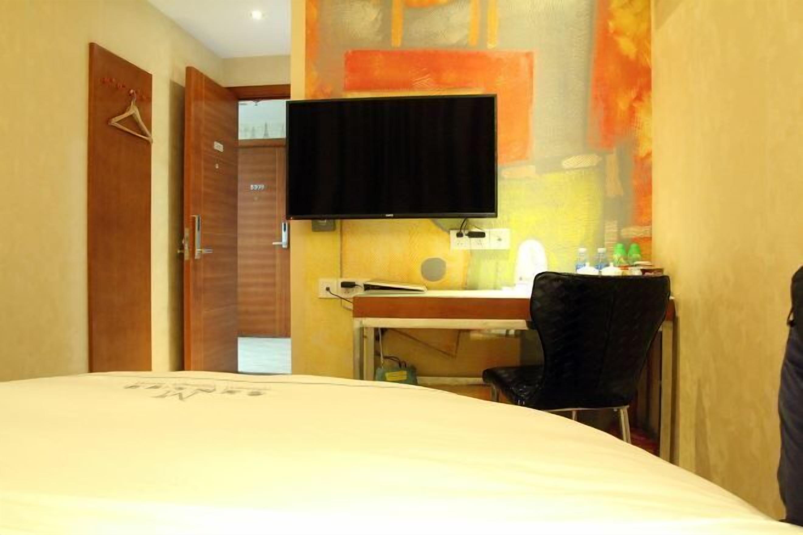 A hotel room with a bed, a desk with a chair, a television, and a door.