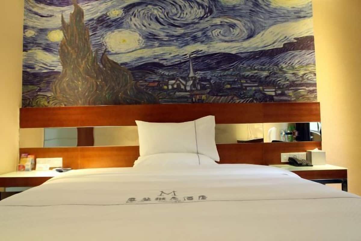 A hotel room with a bed, a nightstand, a desk, and a large painting of a night sky on the wall.