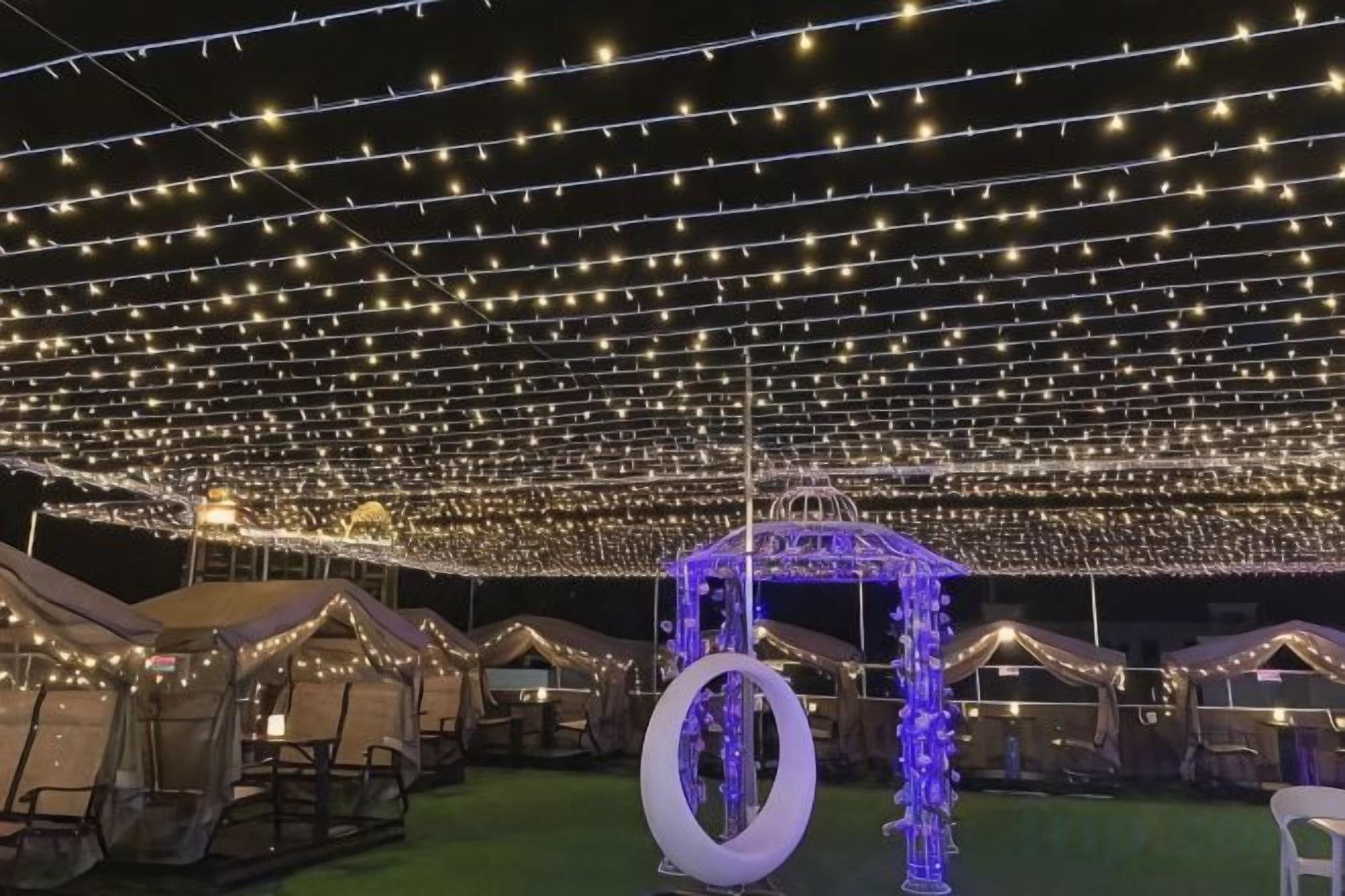Un espacio al aire libre con luces de cuerda, tiendas de campaña y una estructura central con luz azul.