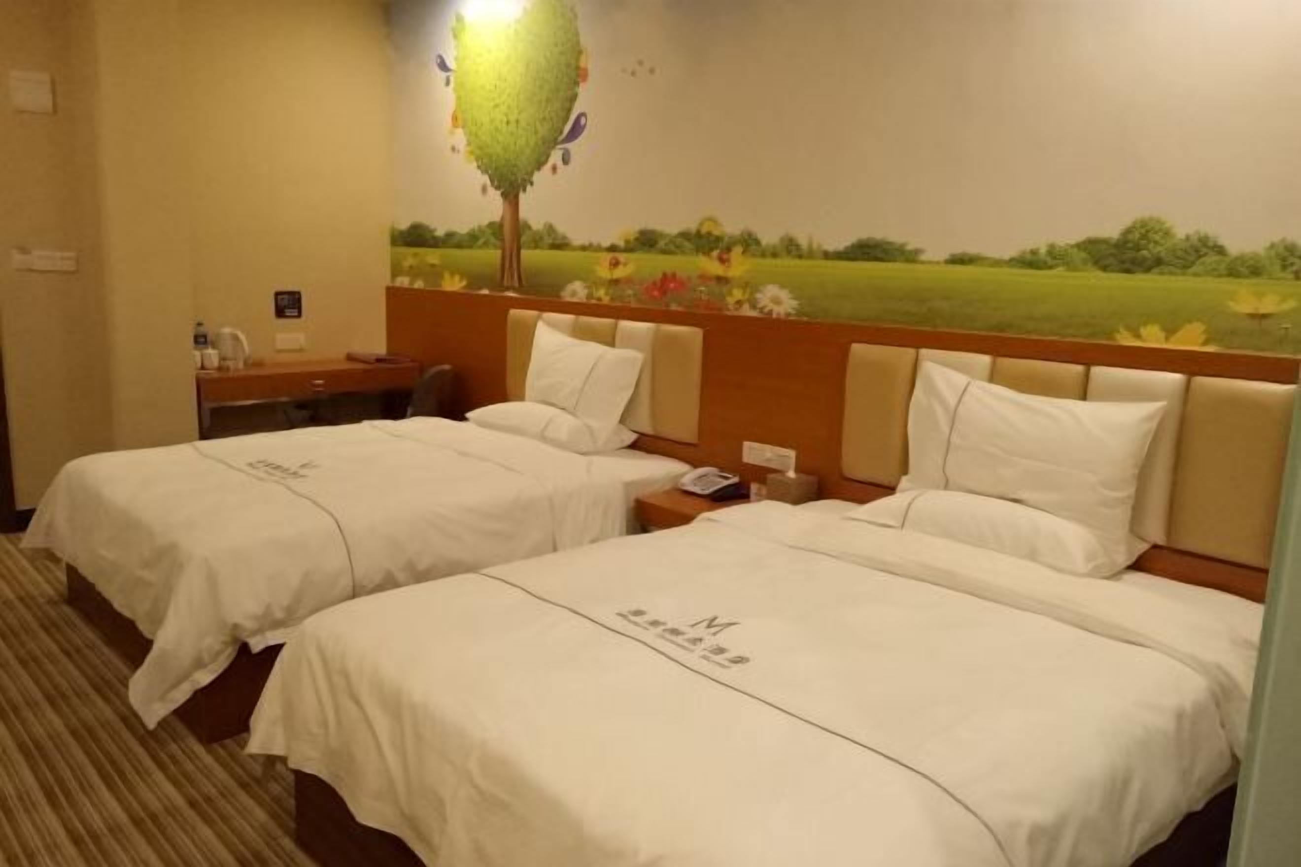 Habitación de hotel con dos camas, una mesita de noche, una lámpara y un mural de un árbol en la pared.