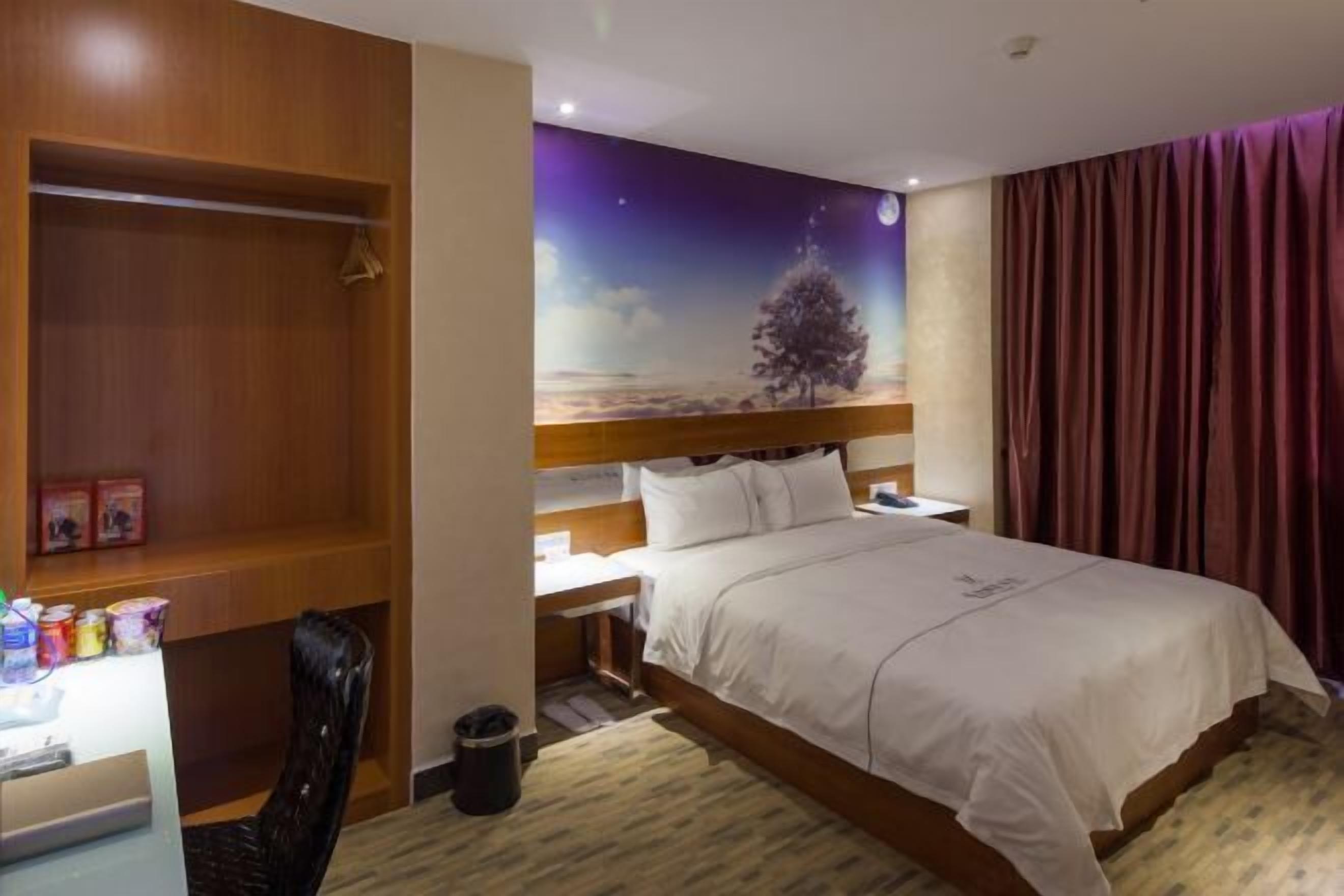 A hotel room with a bed, a desk, a chair, a wardrobe, and a night sky mural on the wall.