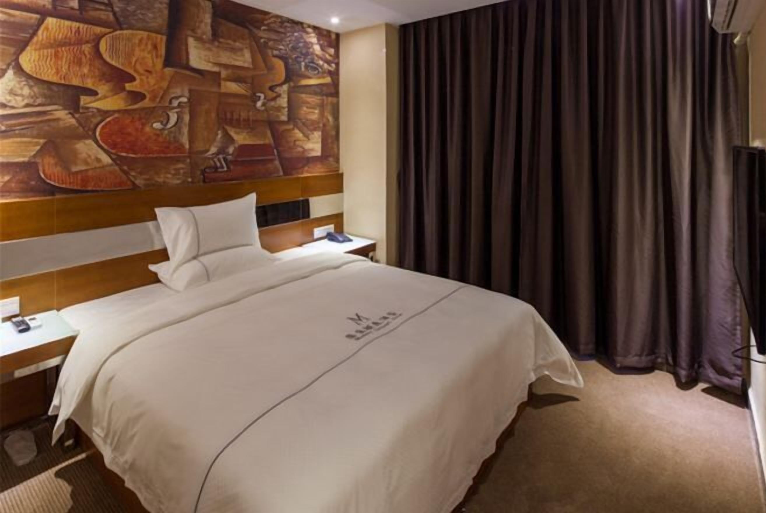 Ein Hotelzimmer mit einem großen Bett, einem Nachttisch, einem Wandbild und einem Fenster mit Vorhängen.