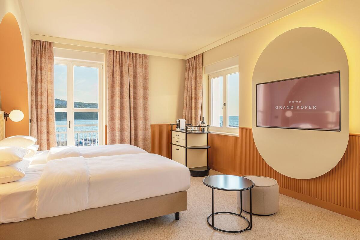 Habitación de hotel con cama, televisión, una mesita y vista al mar.