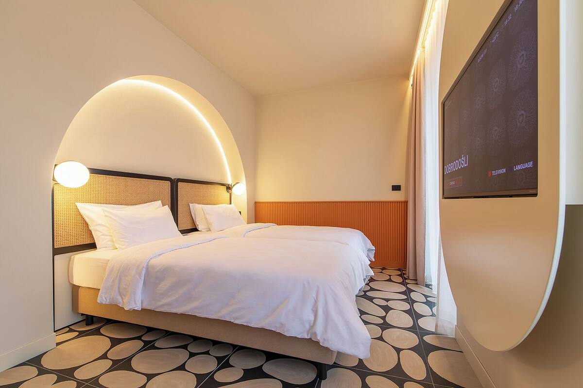 Una habitación de hotel moderna con una cama grande, un diseño de pared curvada, un televisor y una pantalla montada en la pared.