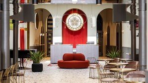 Un vestíbulo moderno con una pared de acento roja, un elemento decorativo circular y zonas de estar con mesas y sillas.