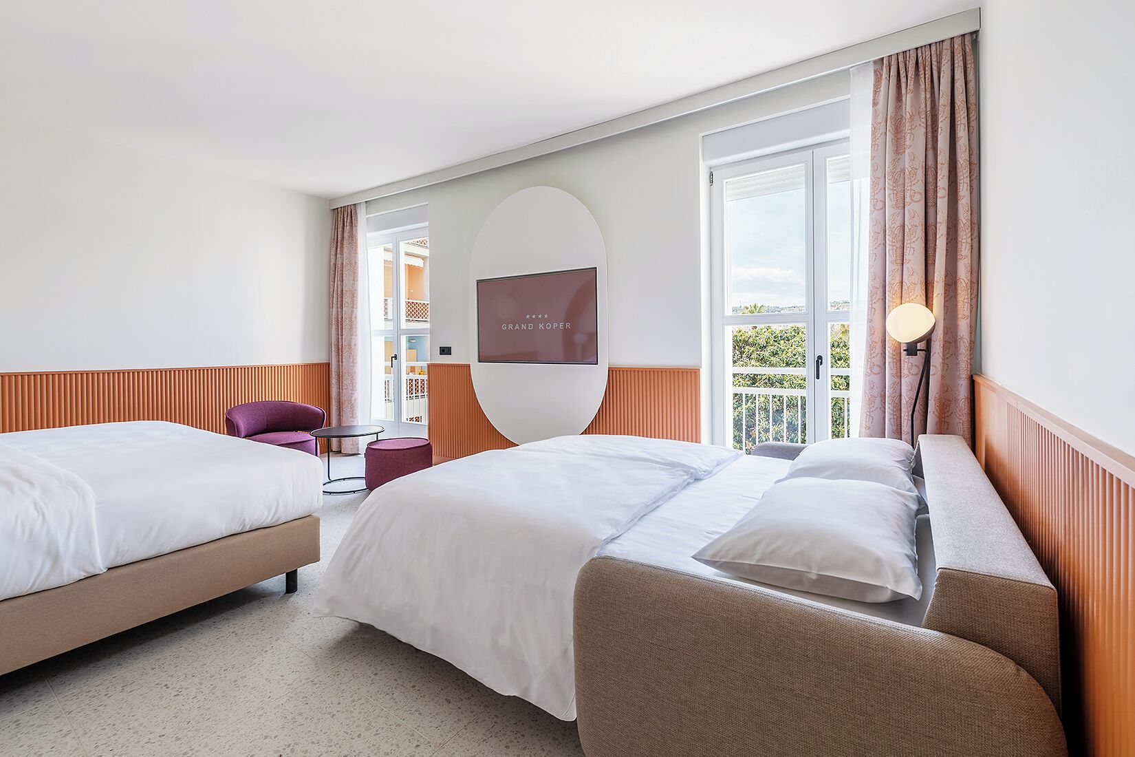 Et hotelværelse med to senge, et opholdsområde, et fjernsyn og balkonudsigt.