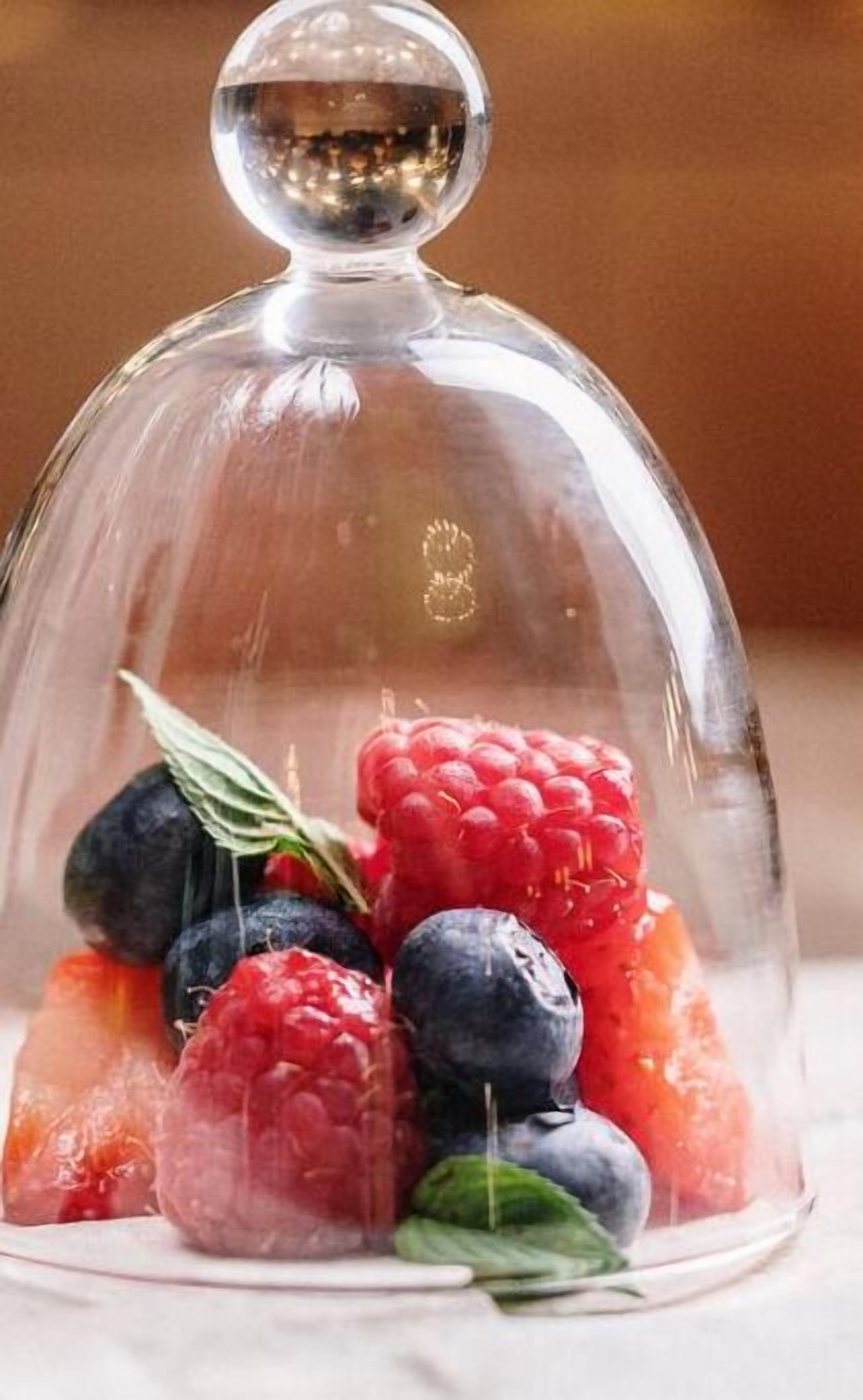 A glass dome over a bowl of fresh berries.