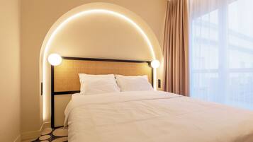 Habitación de hotel con cabecera curva, cama con ropa blanca y vistas al exterior a través de amplios ventanales.