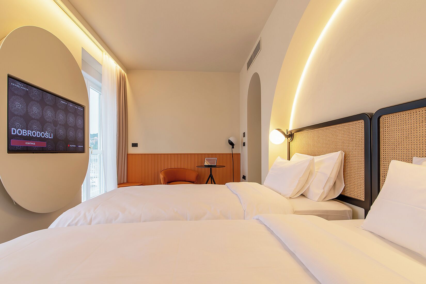 Ein Hotelzimmer mit einem großen Bett, einem an der Wand befestigten Fernseher, einem kleinen Tisch und einem Sessel.