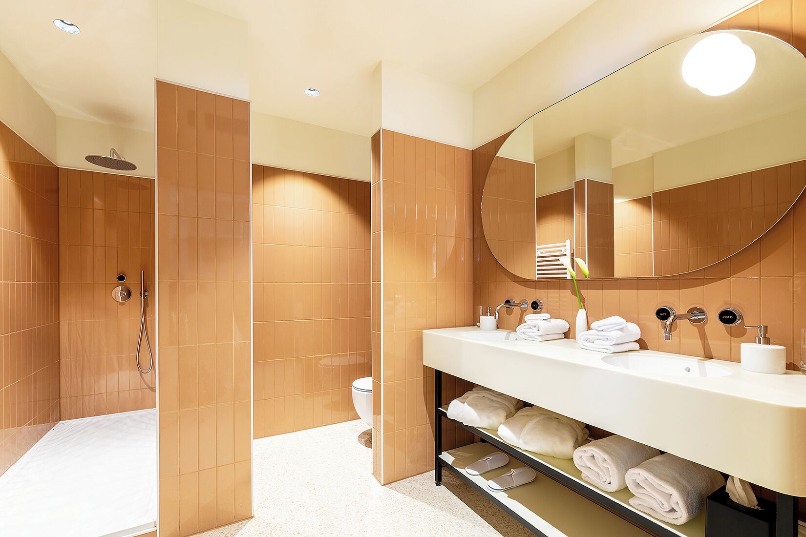 Un baño moderno con ducha a ras de suelo, un espejo grande y un mueble de tocador con toallas y artículos de aseo.