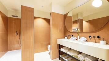 Un baño moderno con ducha a ras de suelo, un espejo grande y un mueble de tocador con toallas y artículos de aseo.