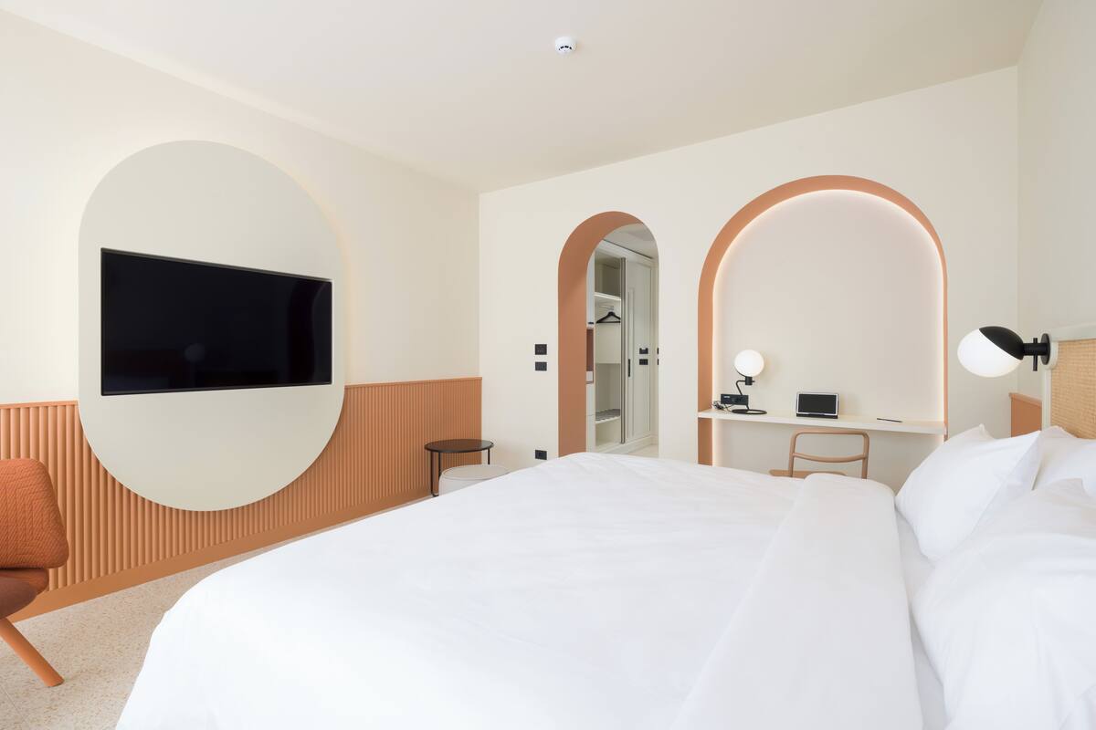 Una habitación de hotel moderna con una cama grande, un televisor de pantalla plana montado en la pared, un escritorio con una silla y un espejo de diseño abovedado.