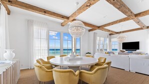 A spacious room with a round table and yellow chairs, a white sofa, and a large TV.