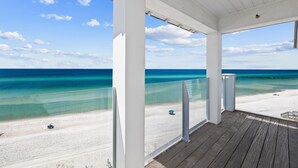 A covered wooden deck overlooking a beach with clear turquoise water and white sand.