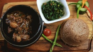 Un plato de estofado, guarnición de vegetales verdes y pan redondo sobre una tabla de madera.