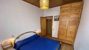 A bedroom with a bed, wooden wardrobe, and a small bedside table with a lamp.