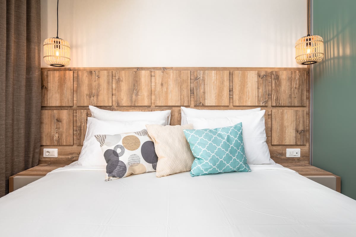 Una cama bien hecha con cabecera de madera, dos lámparas de noche y una variedad de almohadas.