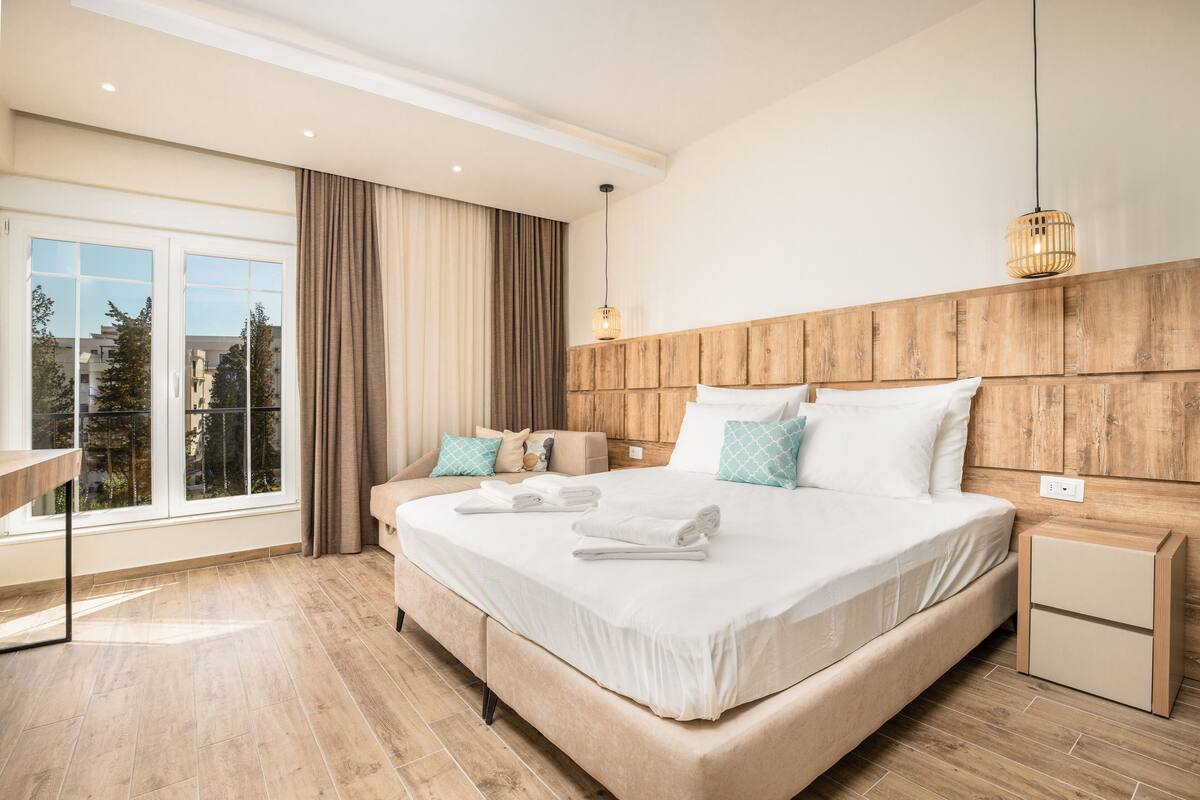 Un dormitorio con una cama grande, una mesita de noche y un ventanal con cortinas.