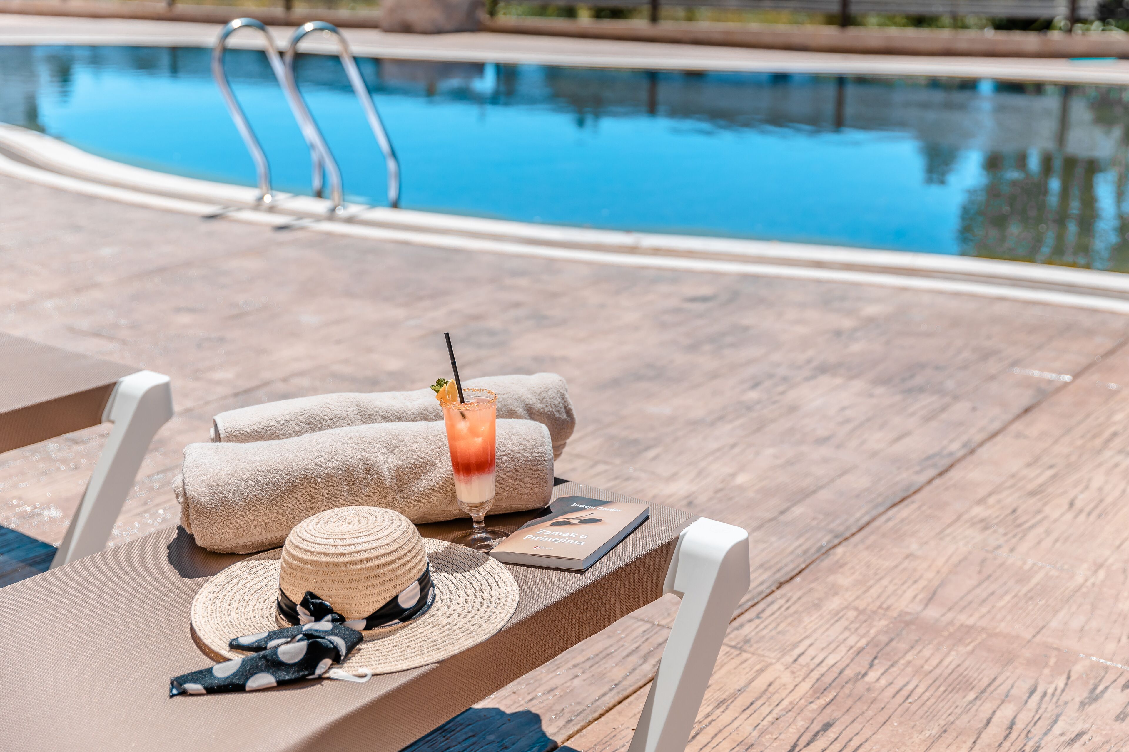 Un espace aménagé au bord de la piscine, avec des chaises longues, des serviettes, une boisson et un livre.