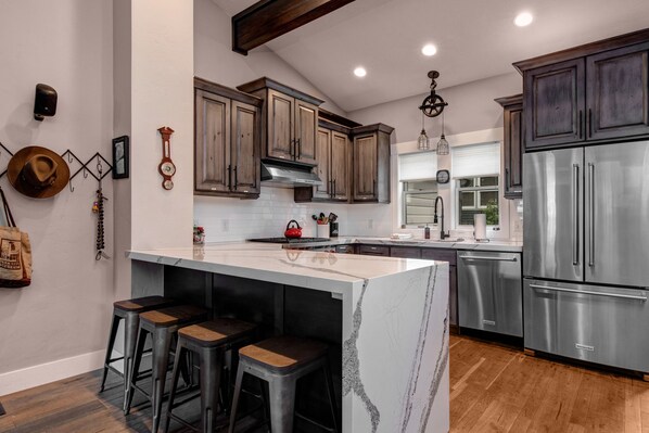 A modern kitchen with a large island, dark wooden cabinets, stainless steel appliances, and a rustic wall clock.