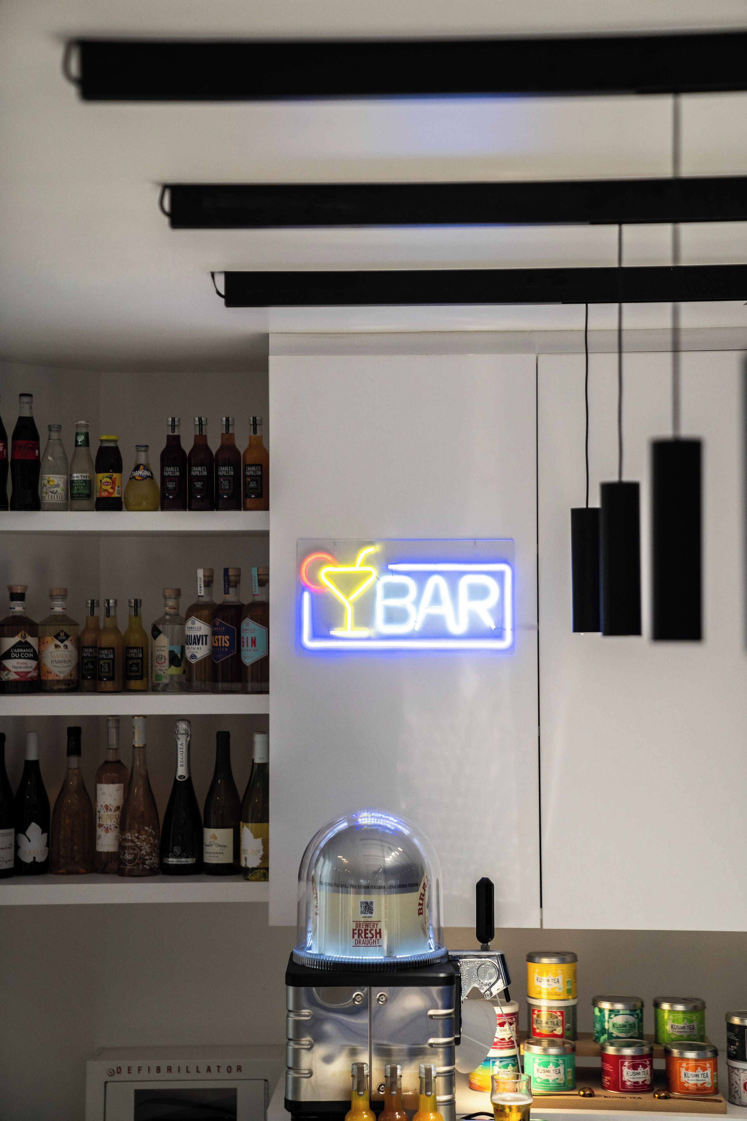 A bar area with a neon sign, shelves of liquor bottles, a coffee machine, and canned beverages.