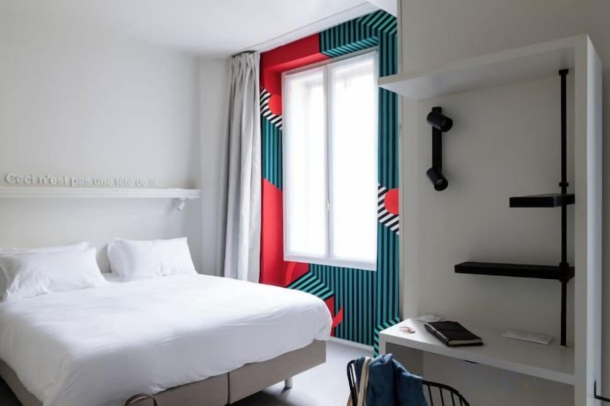 A hotel room with a bed, a desk, and a window with curtains.