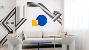 A modern living room with a white sofa, two white armchairs, a blue coffee table, and a geometric wall design. - Graphik Montparnasse (Paris)