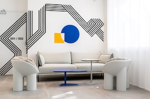 Una sala de estar moderna con un sofá blanco, dos sillones blancos, una mesa de centro azul y un diseño geométrico en la pared.