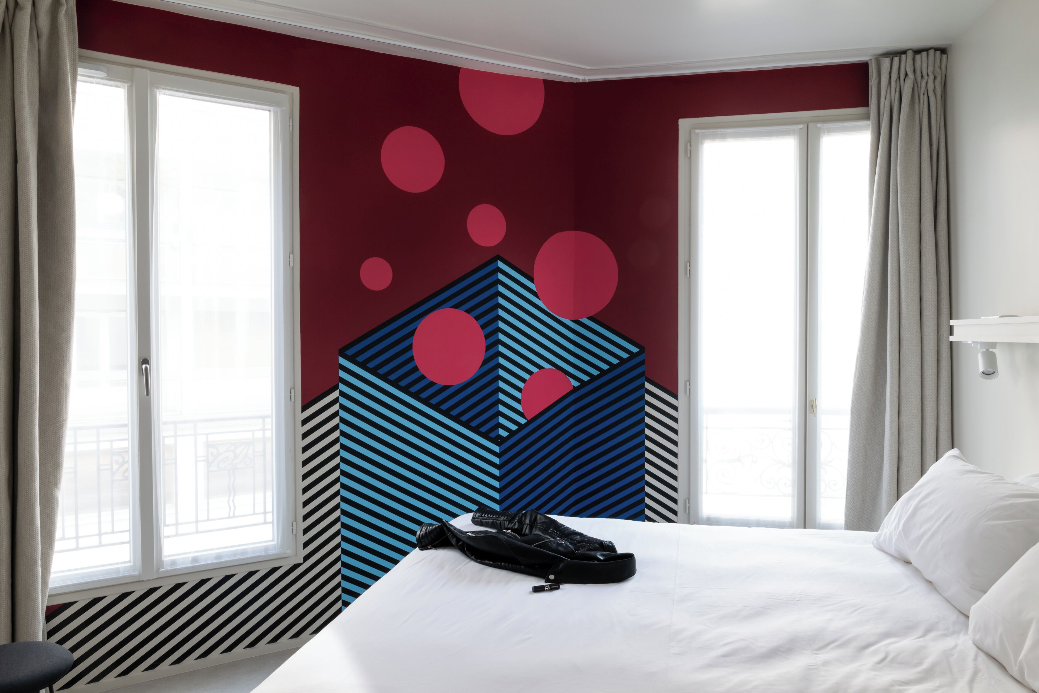 Una habitación de hotel con cama, ventana y un diseño geométrico en la pared.