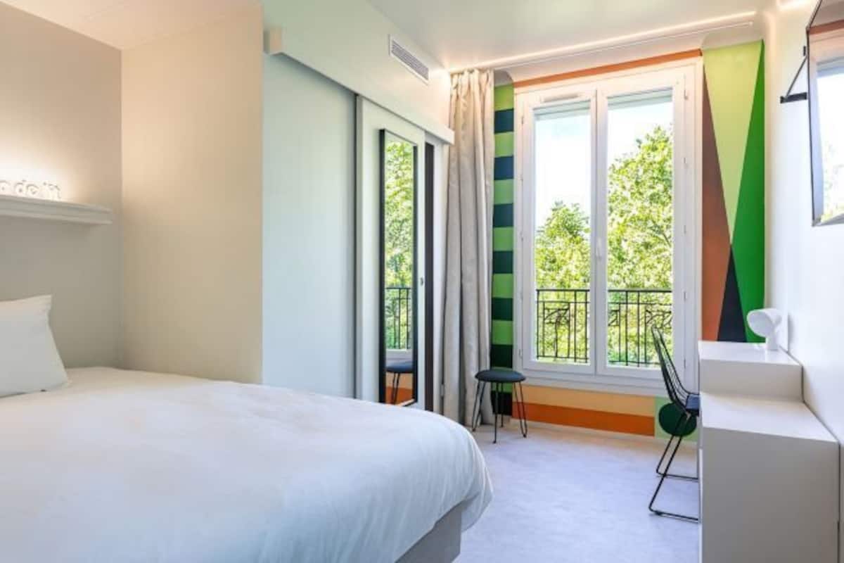 Une chambre dâhĂŽtel comprenant un lit, un bureau, une chaise, une fenĂȘtre avec des rideaux et un balcon.