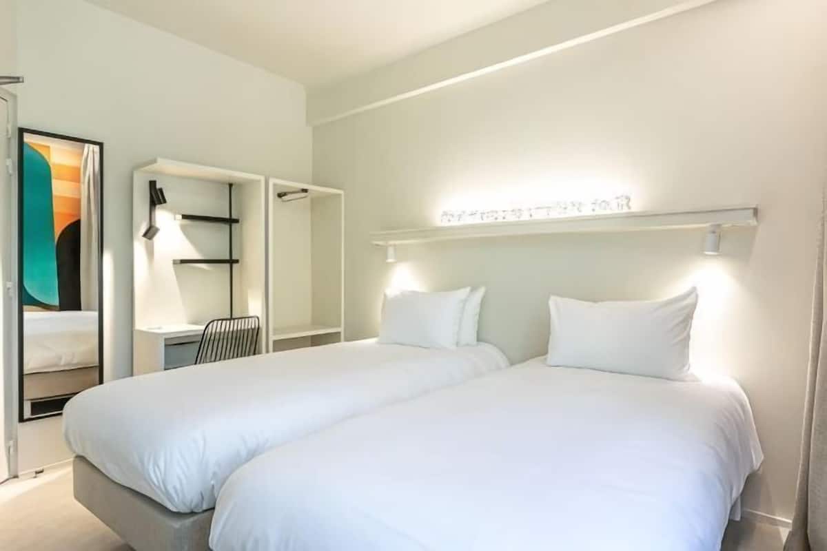 Une chambre d’hôtel avec deux lits, un bureau et une chaise.