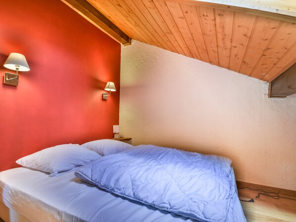 A bedroom with a sloped ceiling, red walls, and a bed with white and blue bedding.
