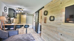 A modern kitchen with a wooden wall, a bar area, and a seating area with a sofa and chairs. - Renovated Studio with Cabin in Village Center, Near Ski Lifts - Les Gets (Les Gets)