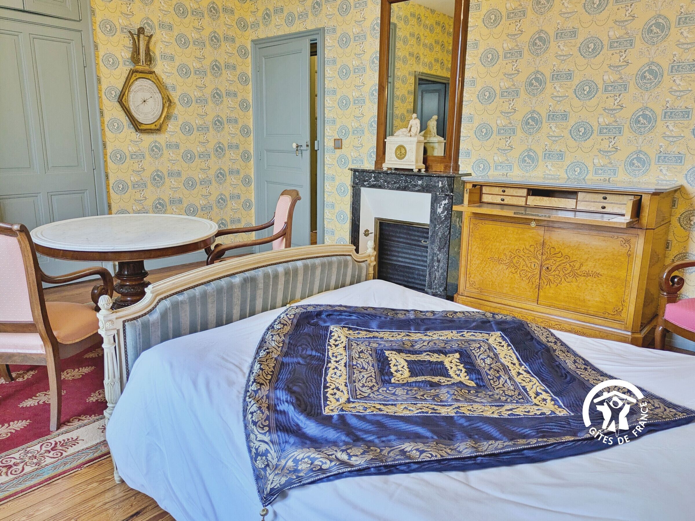 Ein traditionell eingerichteter Raum mit einem Bett, einem runden Tisch, einem Stuhl, einer Kommode und einem Kamin.