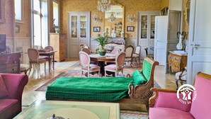Un salon spacieux comprenant un coin repas, un lustre et un canapé vert.