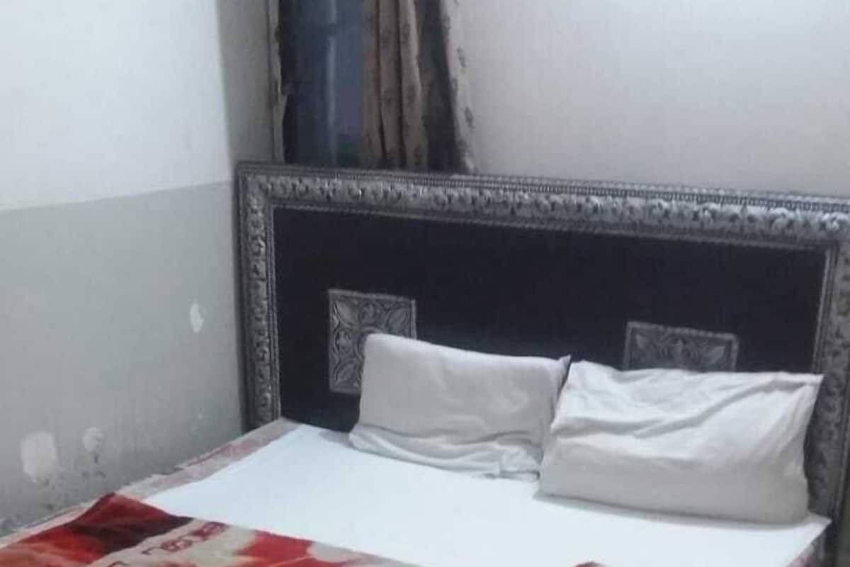 A bed with a patterned bedspread, a headboard, and a plain wall.