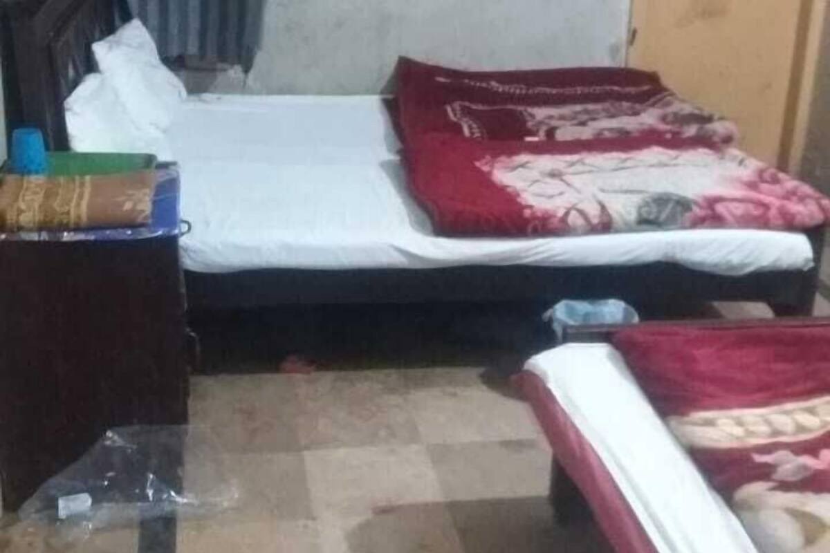 A small, compact room with two single beds, a wooden headboard, a small table, and a curtain.