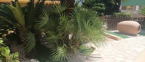 A garden with palm trees, a stone pathway, and a large clay pot.