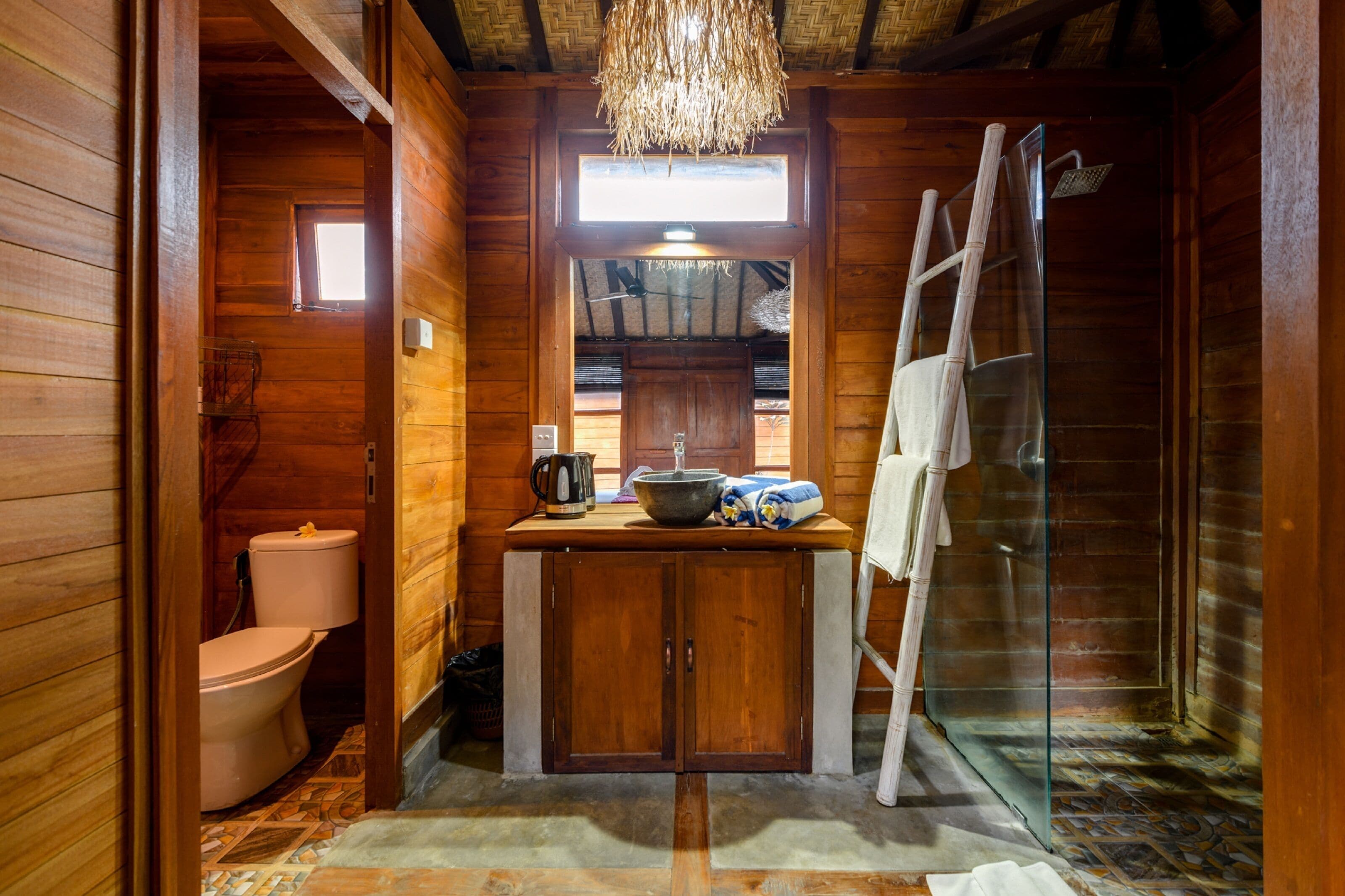 A wooden cabin bathroom with a toilet, sink, and shower.