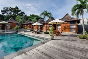 A poolside area with wooden deck, lounge chairs, umbrellas, and a pool. - Turtle Villas Canggu (Tibubeneng)