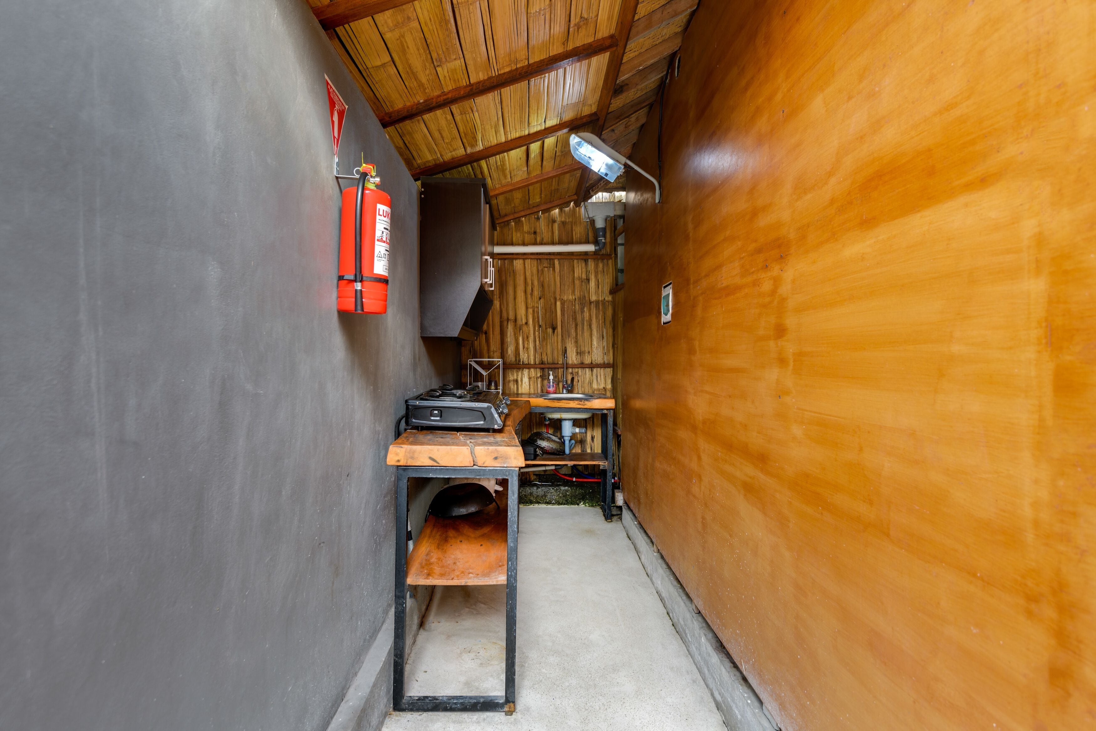 A narrow hallway with a wooden ceiling, a fire extinguisher, a table with a sink, and a bench.